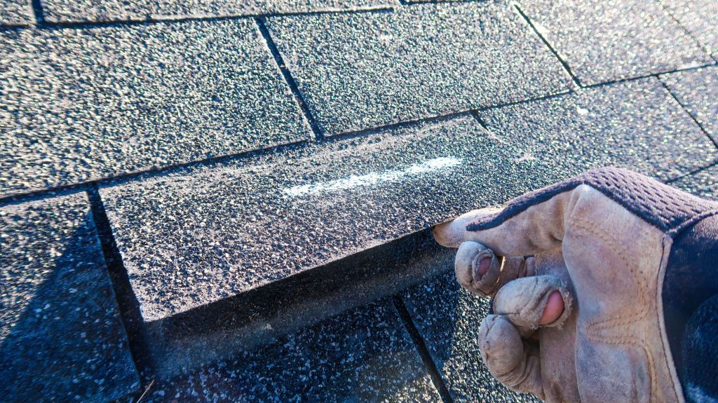 Roofer inspecting a damaged shingle on a roof