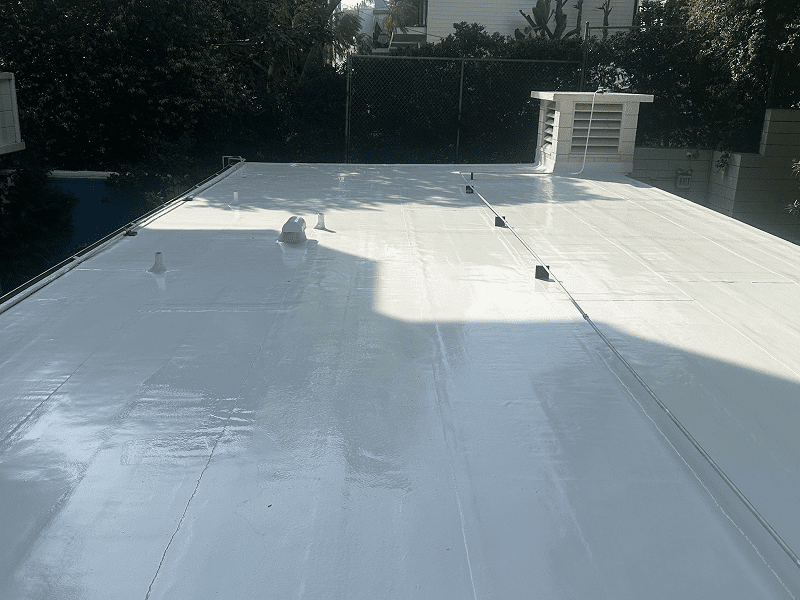Workers applying white roofing material on flat roof under sunny sky.