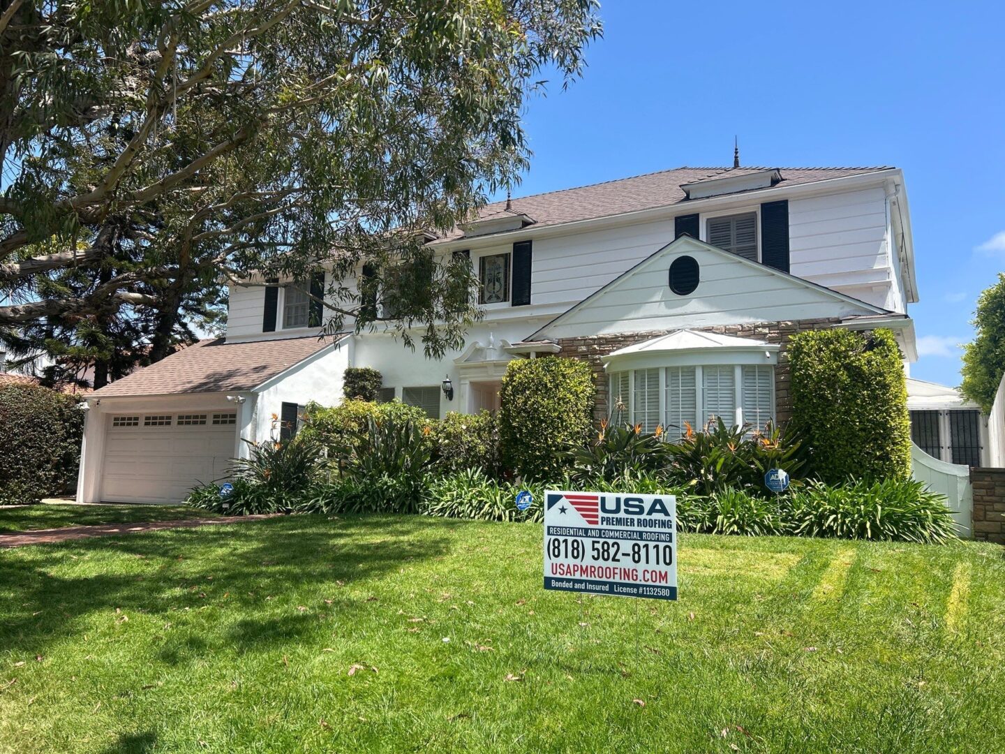 A two-story white house with a large green lawn and a real estate sign.