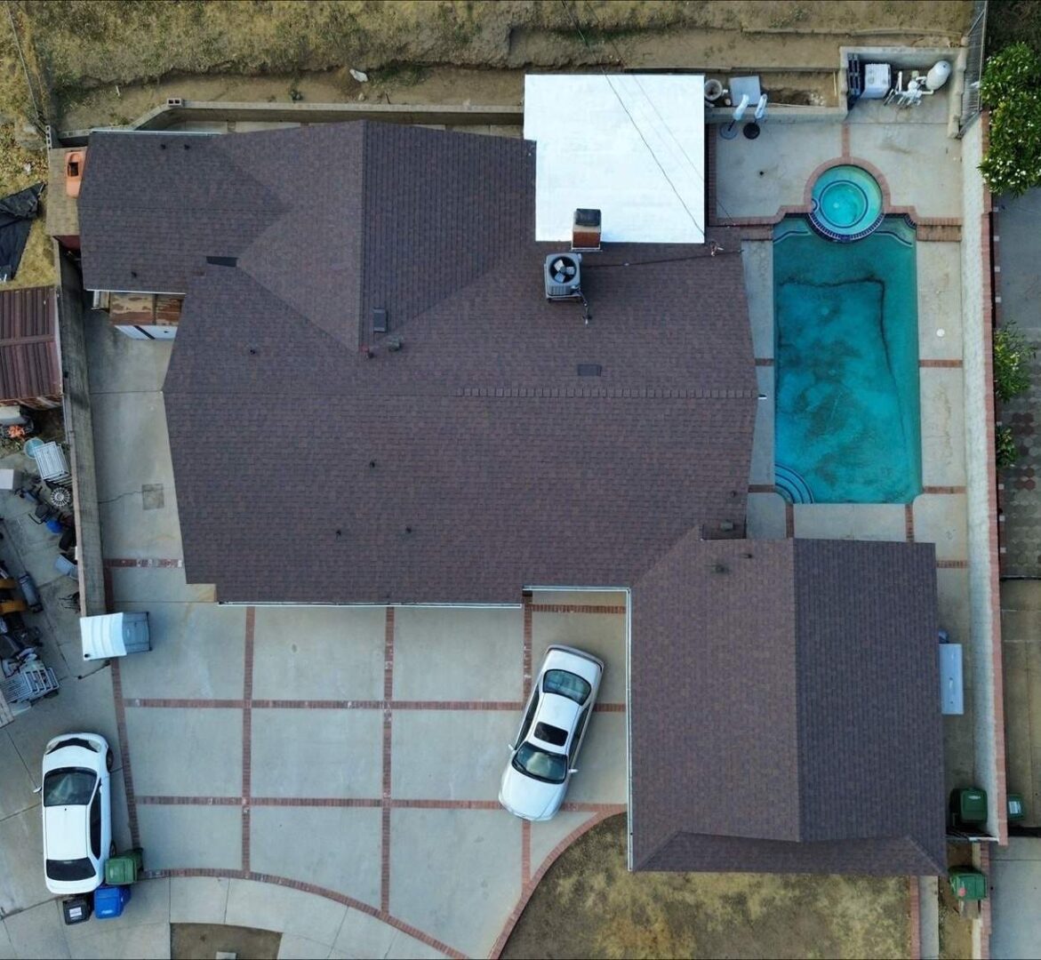 Aerial view of a house with a driveway, cars, and a swimming pool.