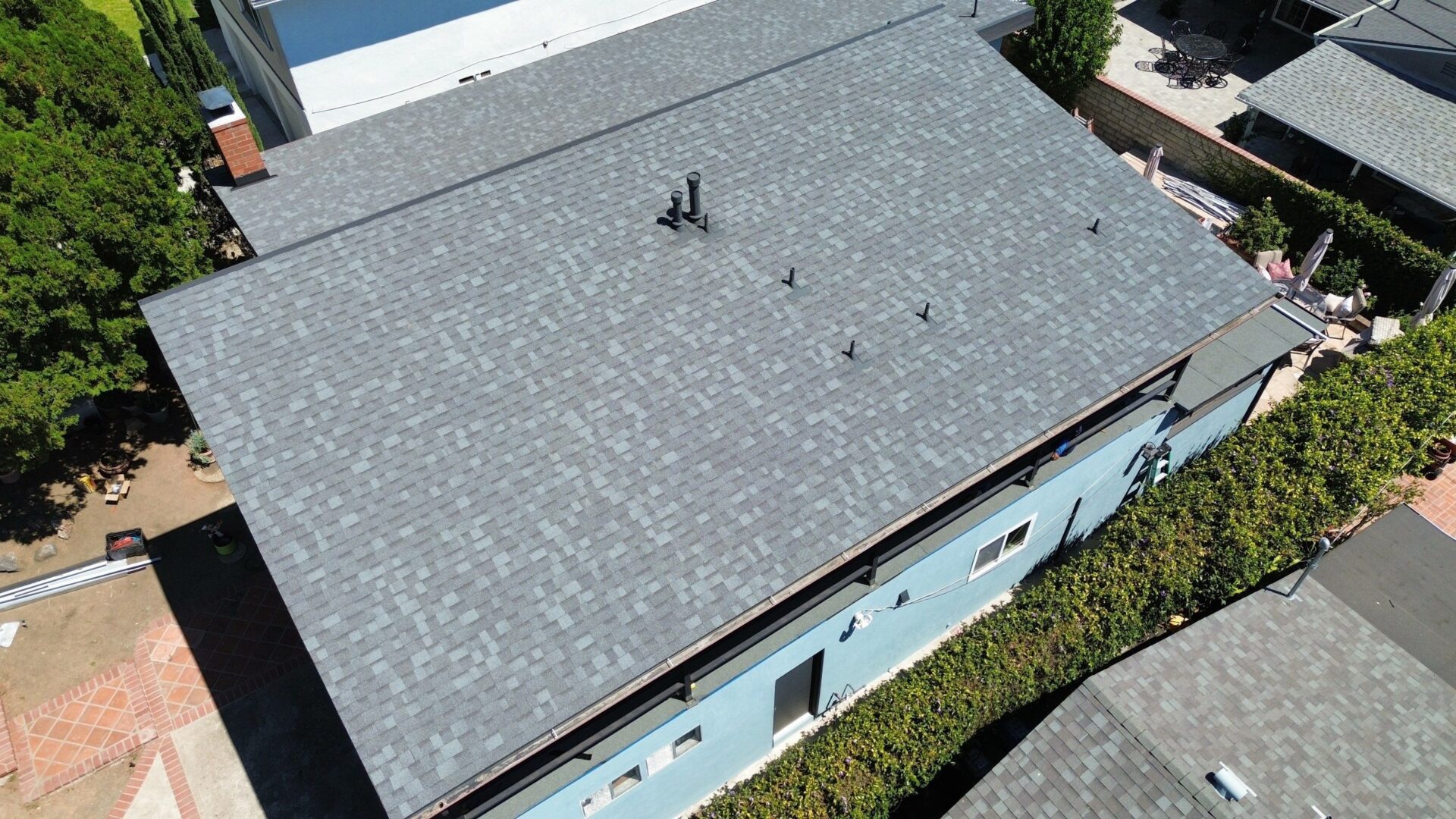 A gray shingled roof with vents and a chimney on a blue house.