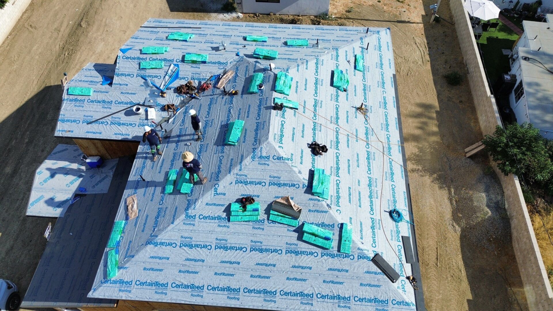Workers installing roofing materials on a house under construction.