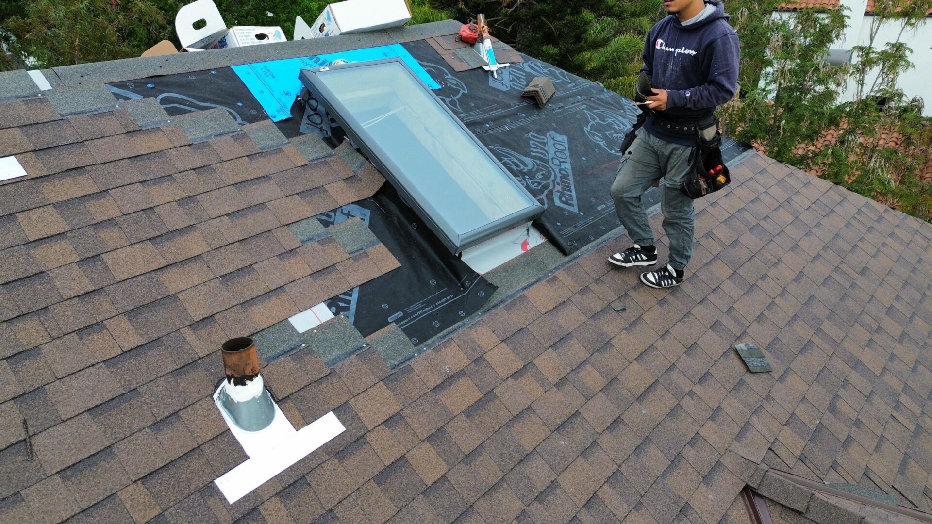 A worker installing a skylight on a brown shingled roof.
