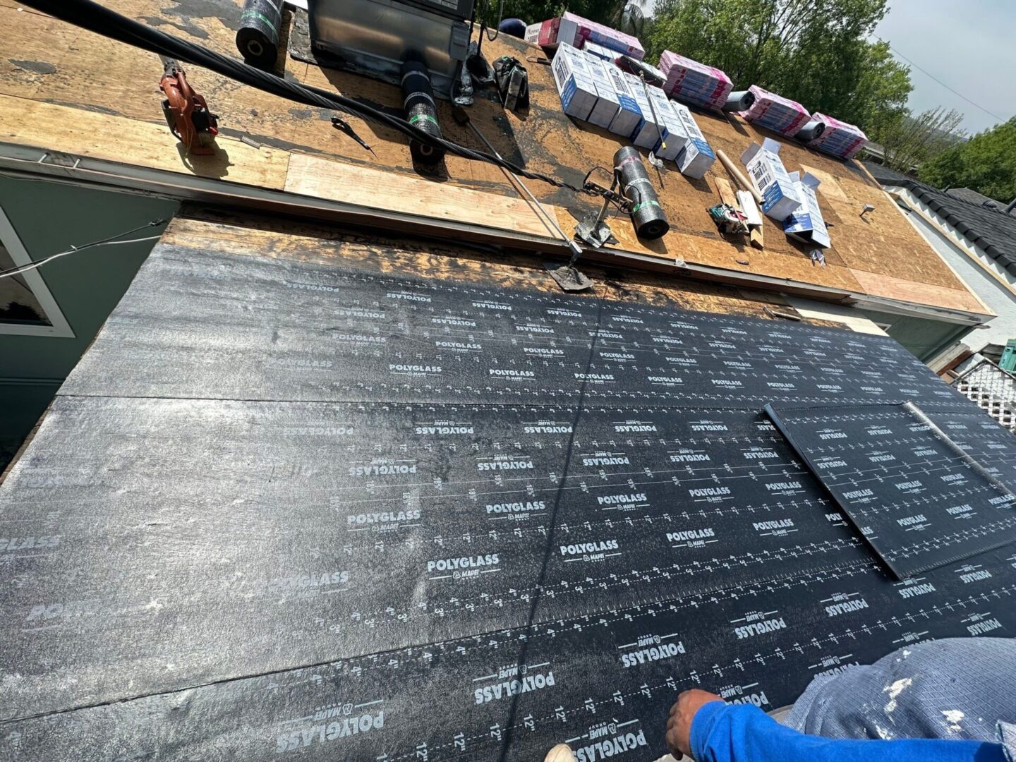 Workers installing roofing underlayment with tools on a roof.