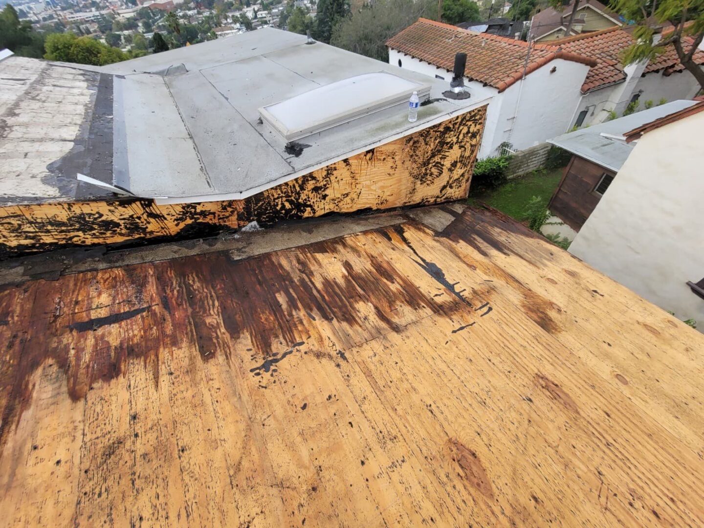 Rust and corrosion on a metal rooftop with surrounding houses.