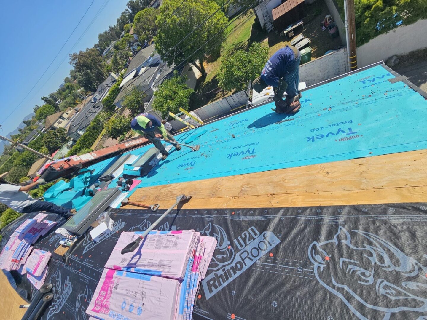 Workers install blue waterproof roofing underlayment on a house roof.