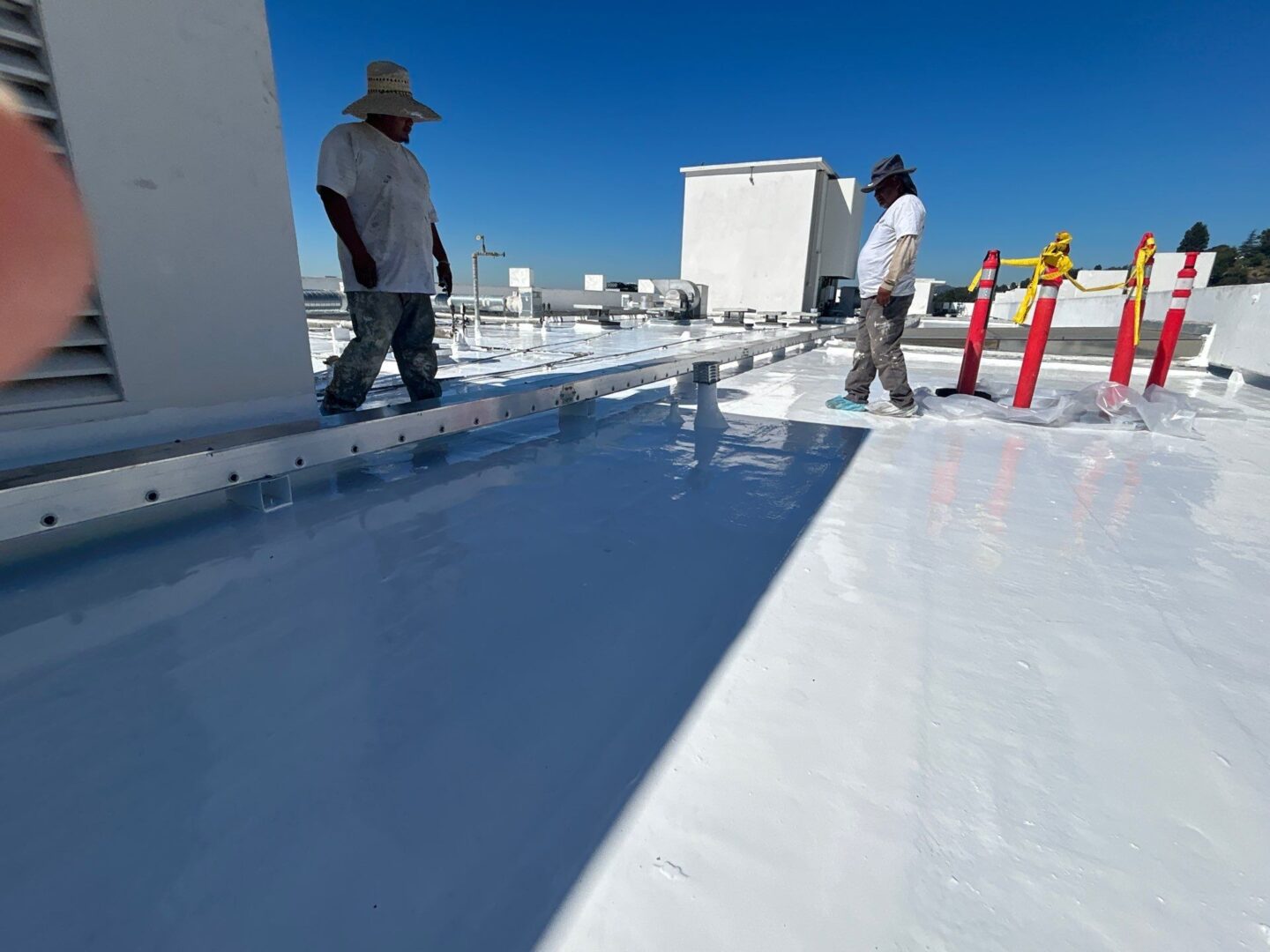 Workers applying white coating on a rooftop under clear sky.