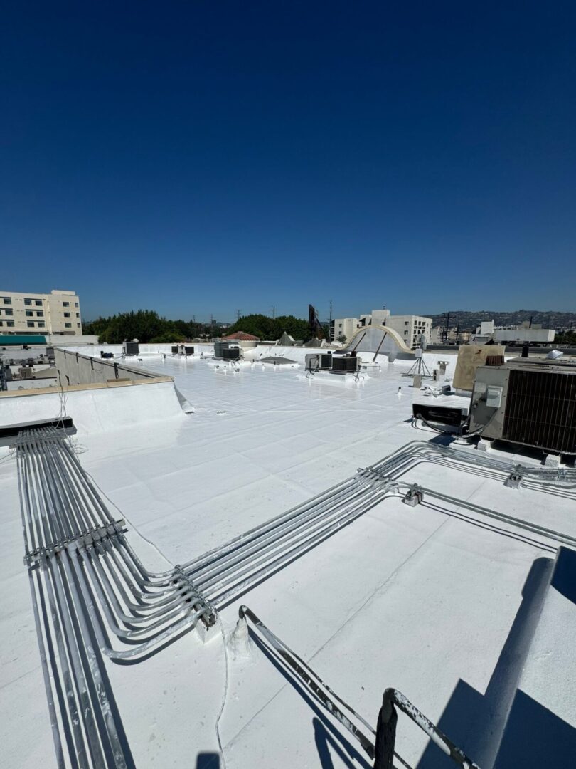 White rooftop with multiple pipes and air conditioning units under clear blue sky.