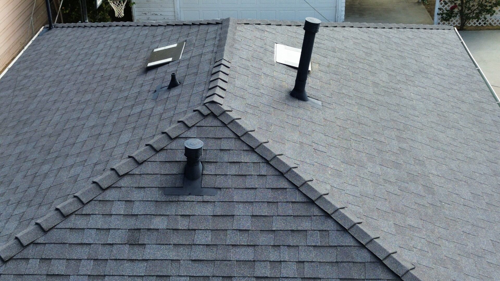 A rooftop with grey shingles and two ventilation pipes visible.
