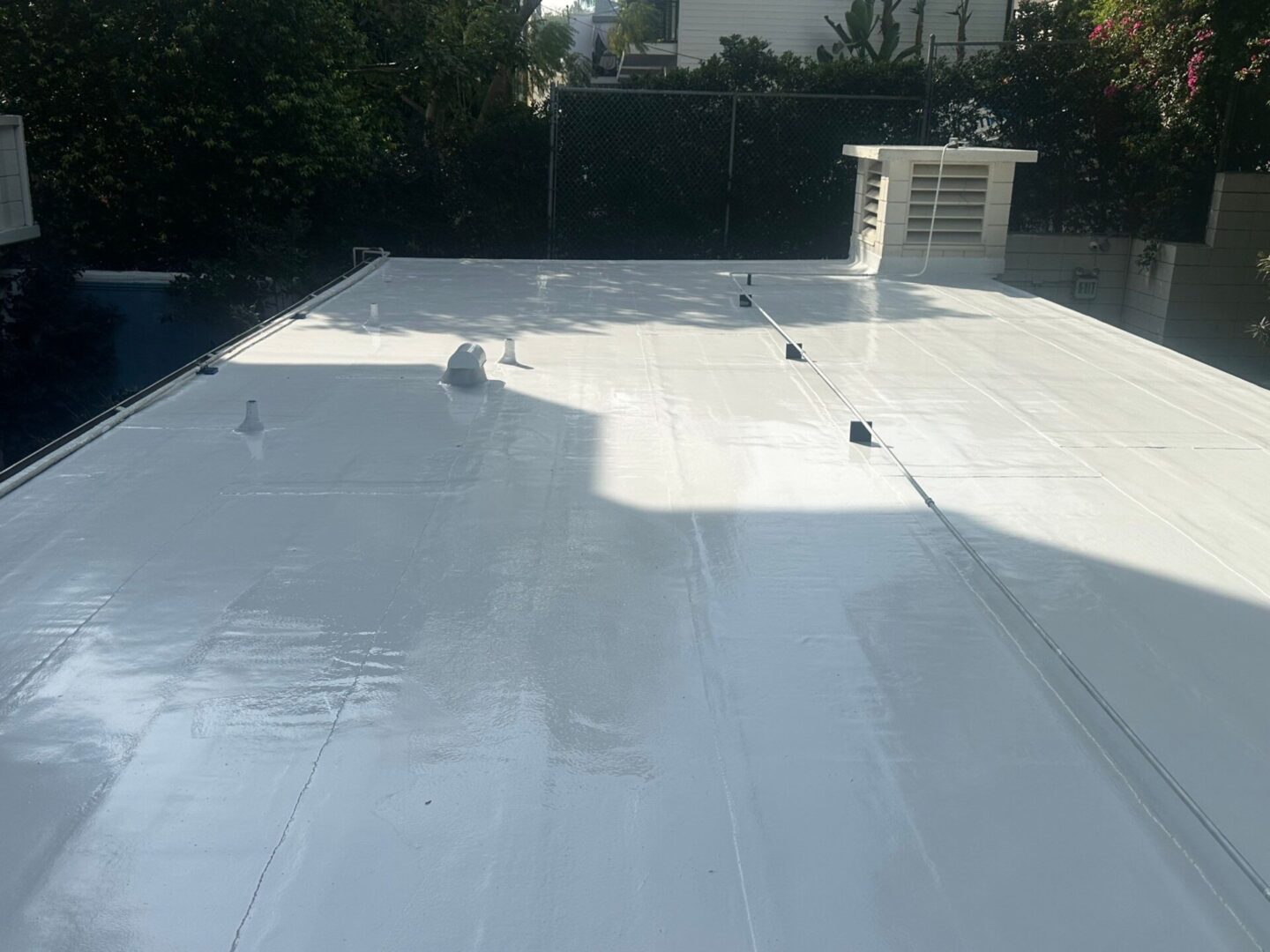 A flat roof coated with a reflective white material under sunlight.