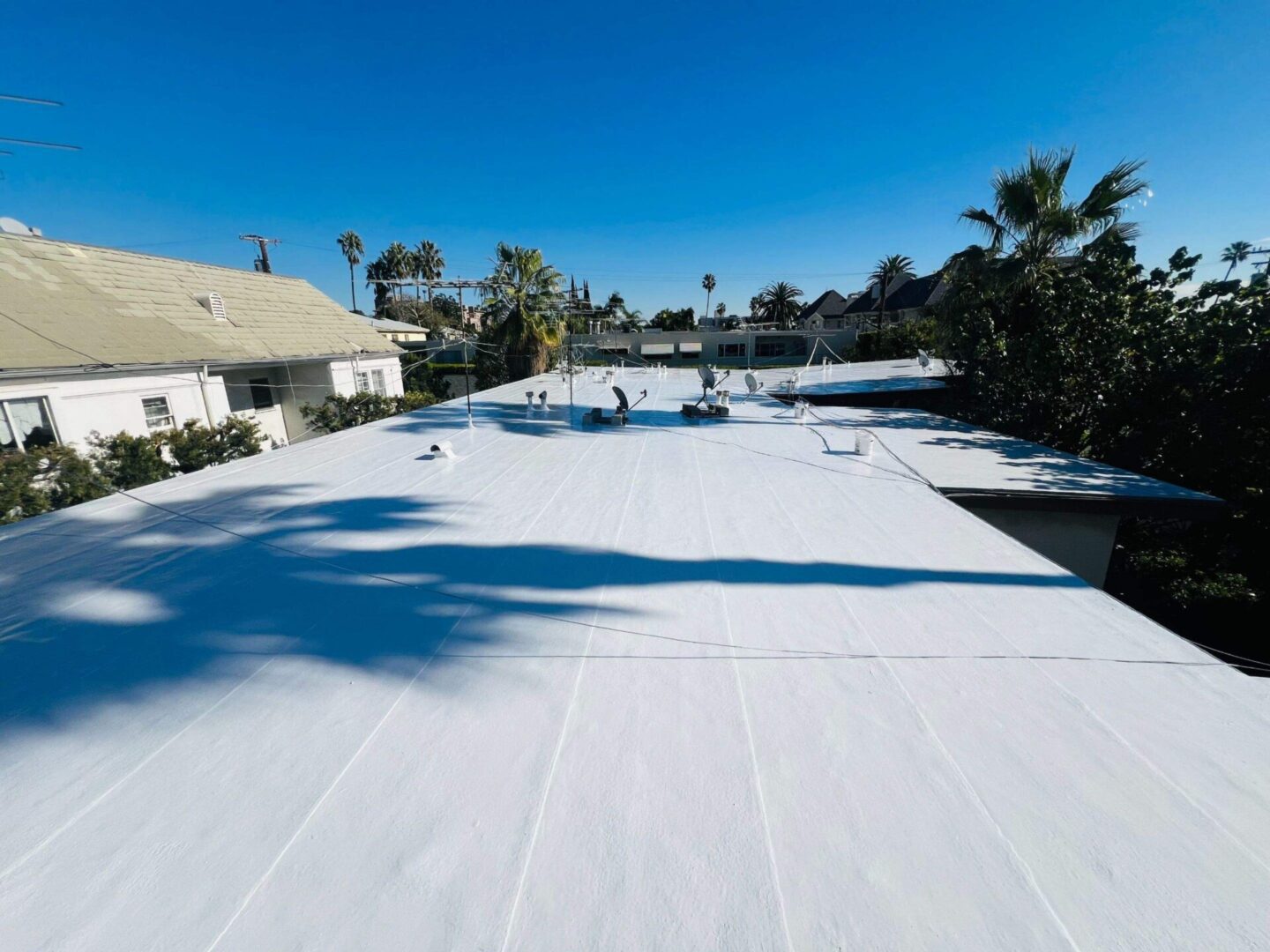 A large flat roof covered with a white waterproof membrane under clear blue skies.