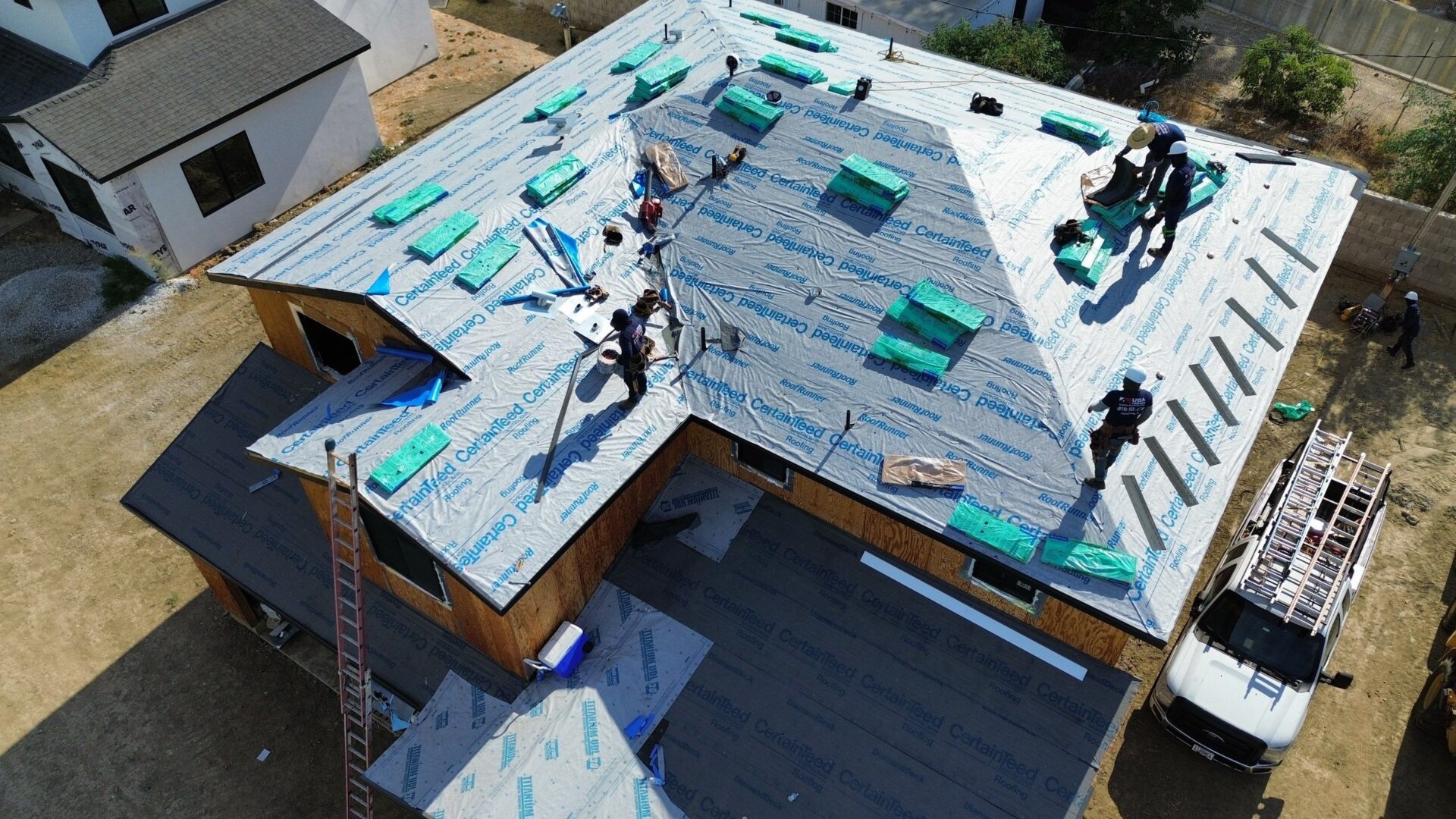 Workers installing roofing material on a house under construction.