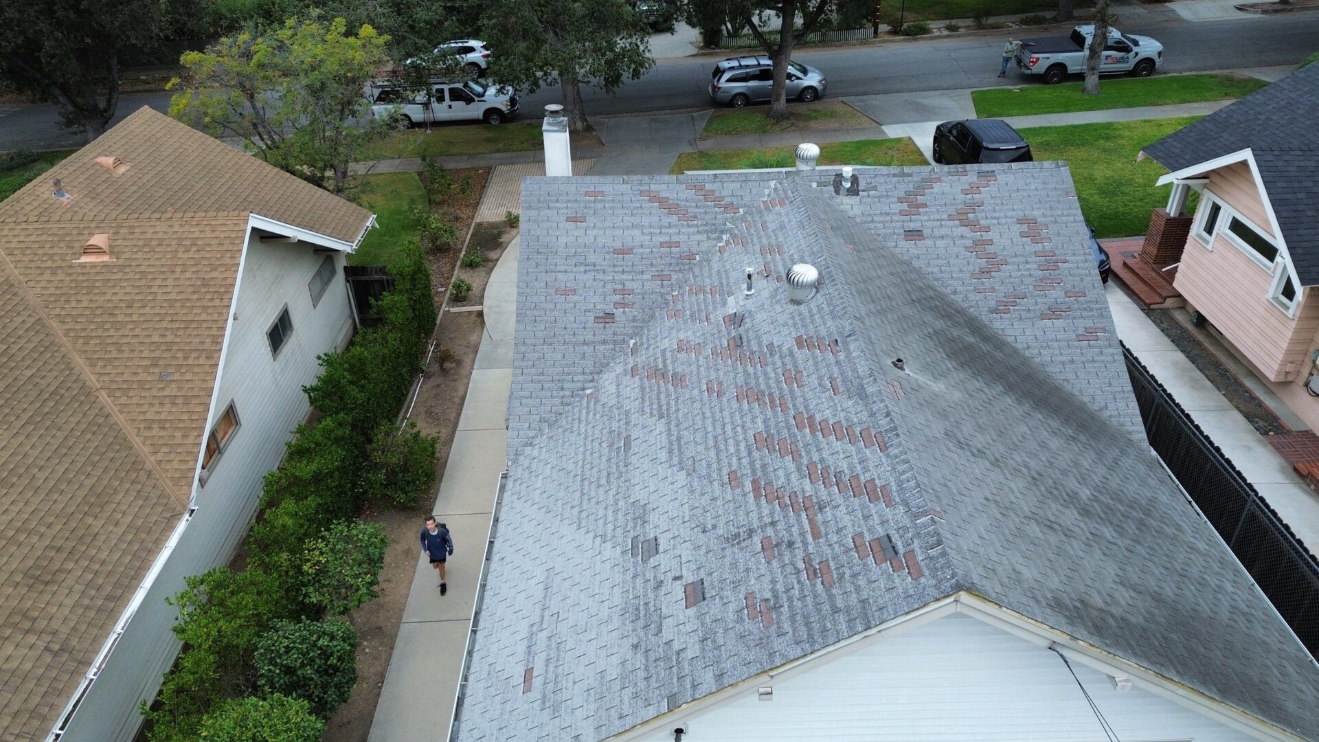 A person walks on a sidewalk beside a house with a large, weathered roof.