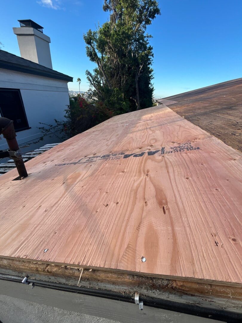 A person walks on a newly installed plywood roof under a clear blue sky.