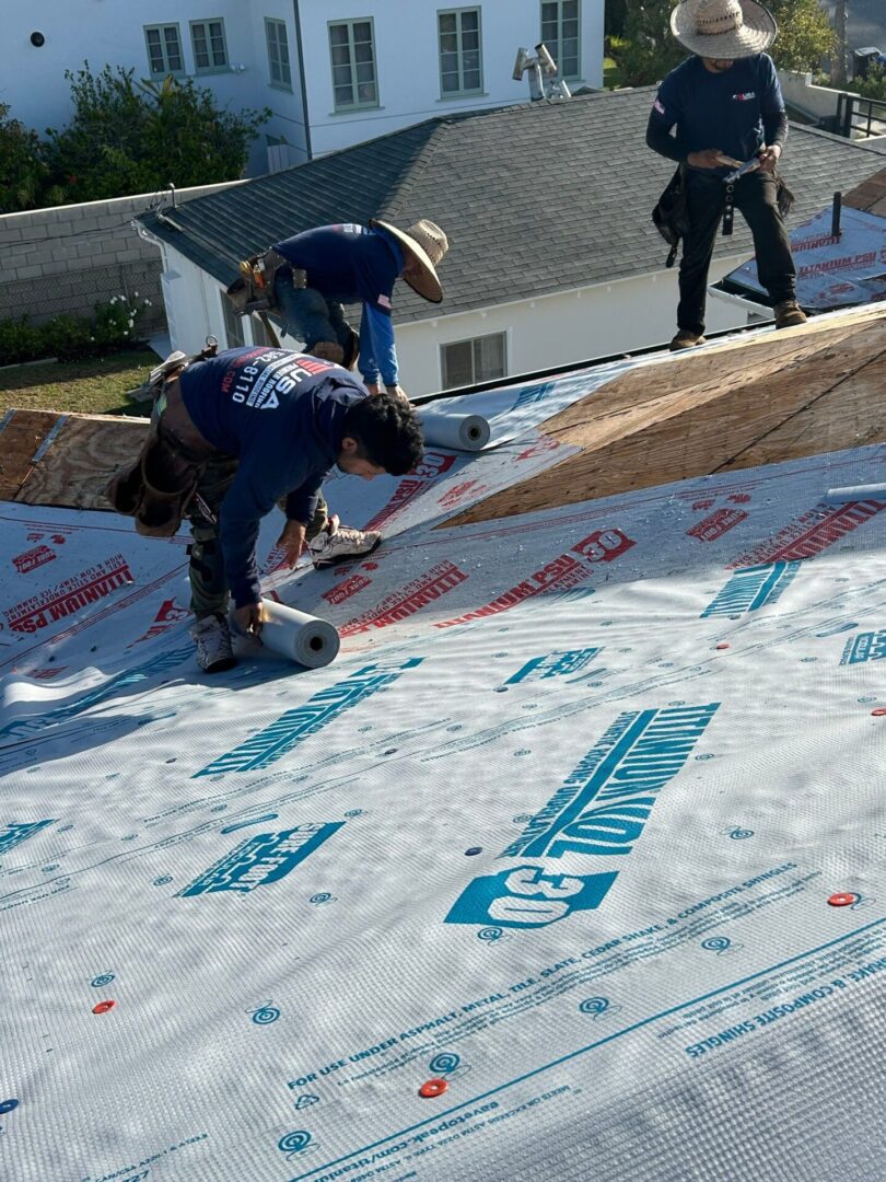 Workers installing roofing underlayment on a house roof.