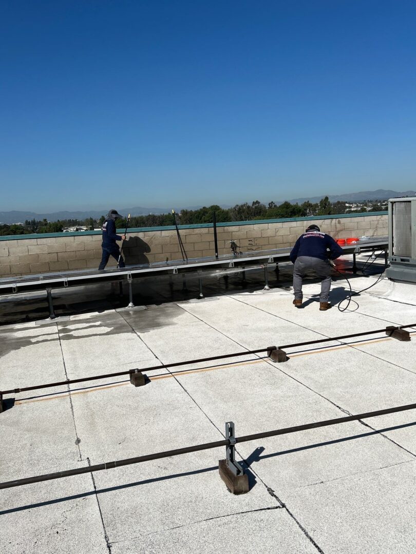 Two workers constructing a building roof under clear blue sky.