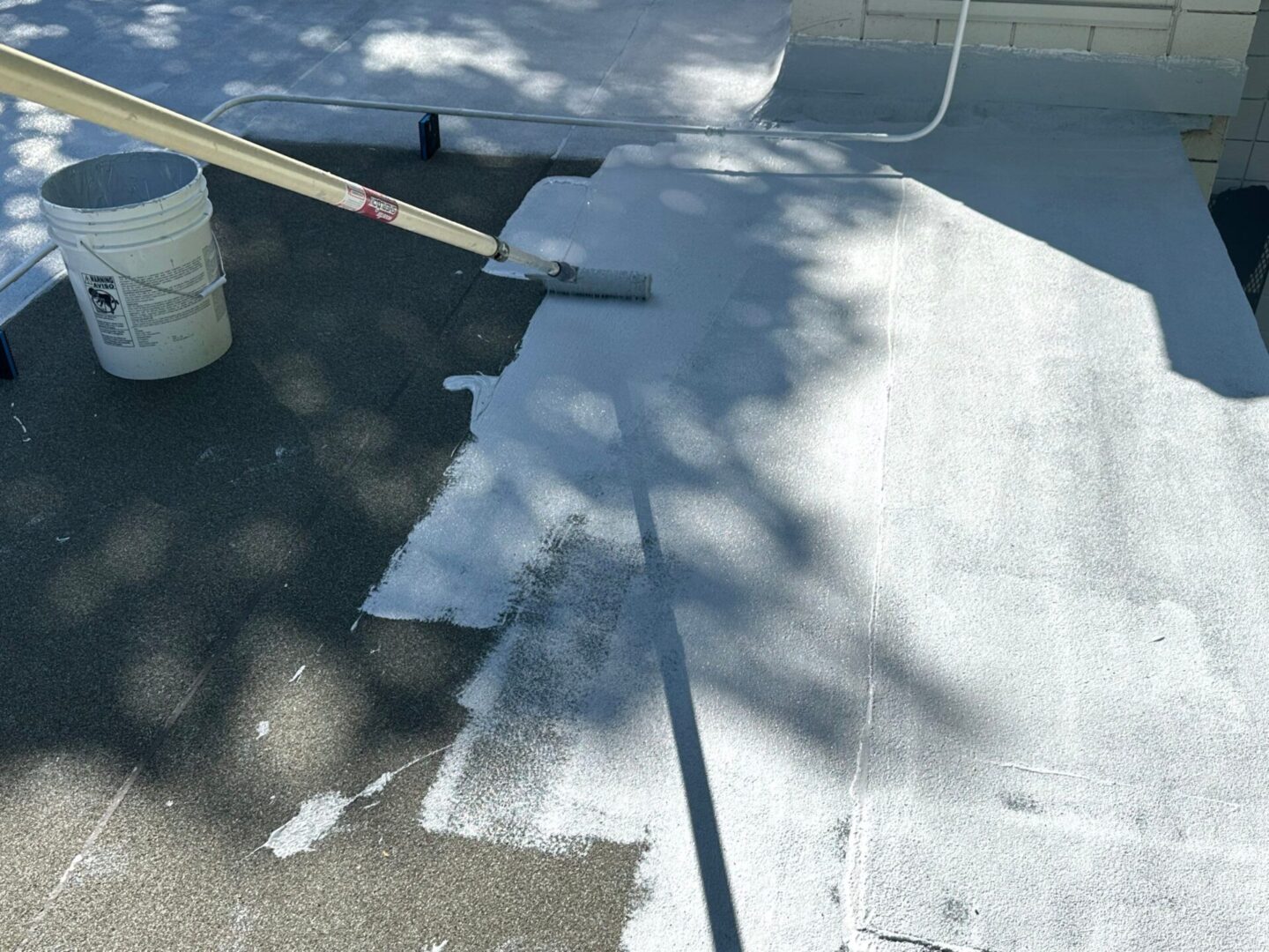 Person applying white paint on pavement with a roller.