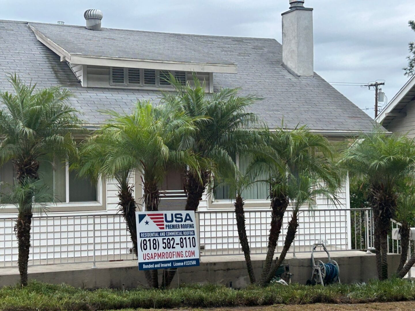 House with a USA Real Estate sign and palm trees in front.