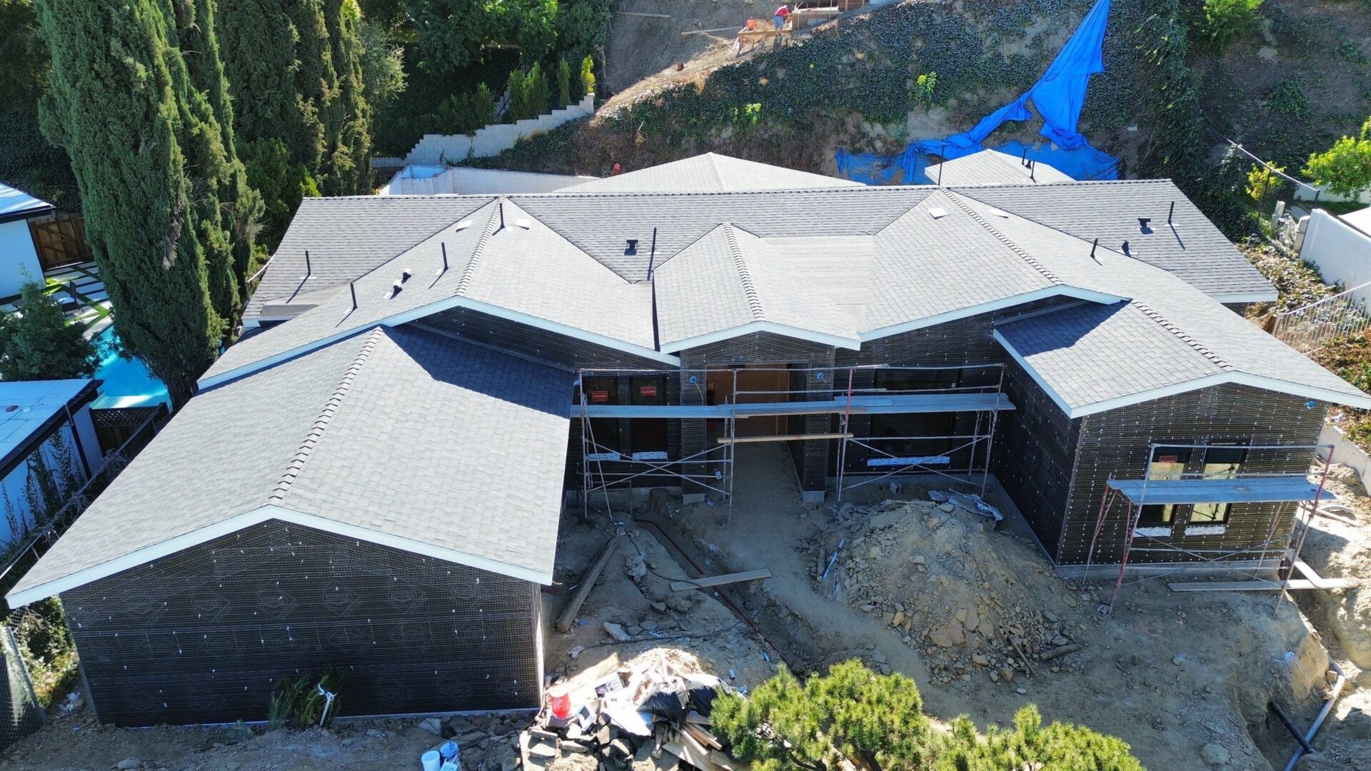 Aerial view of a large house under construction with a complex roof design.