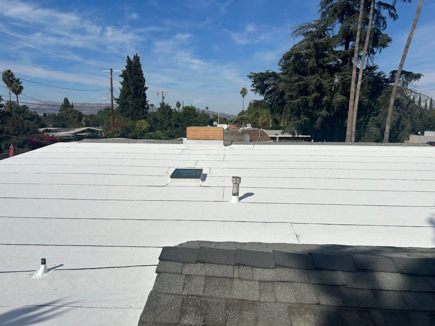 A white rooftop with vents and a chimney under a partly cloudy sky.