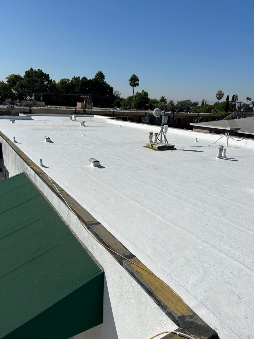 A large white reflective roofing installation on a flat surface with HVAC units and palm trees in the background.