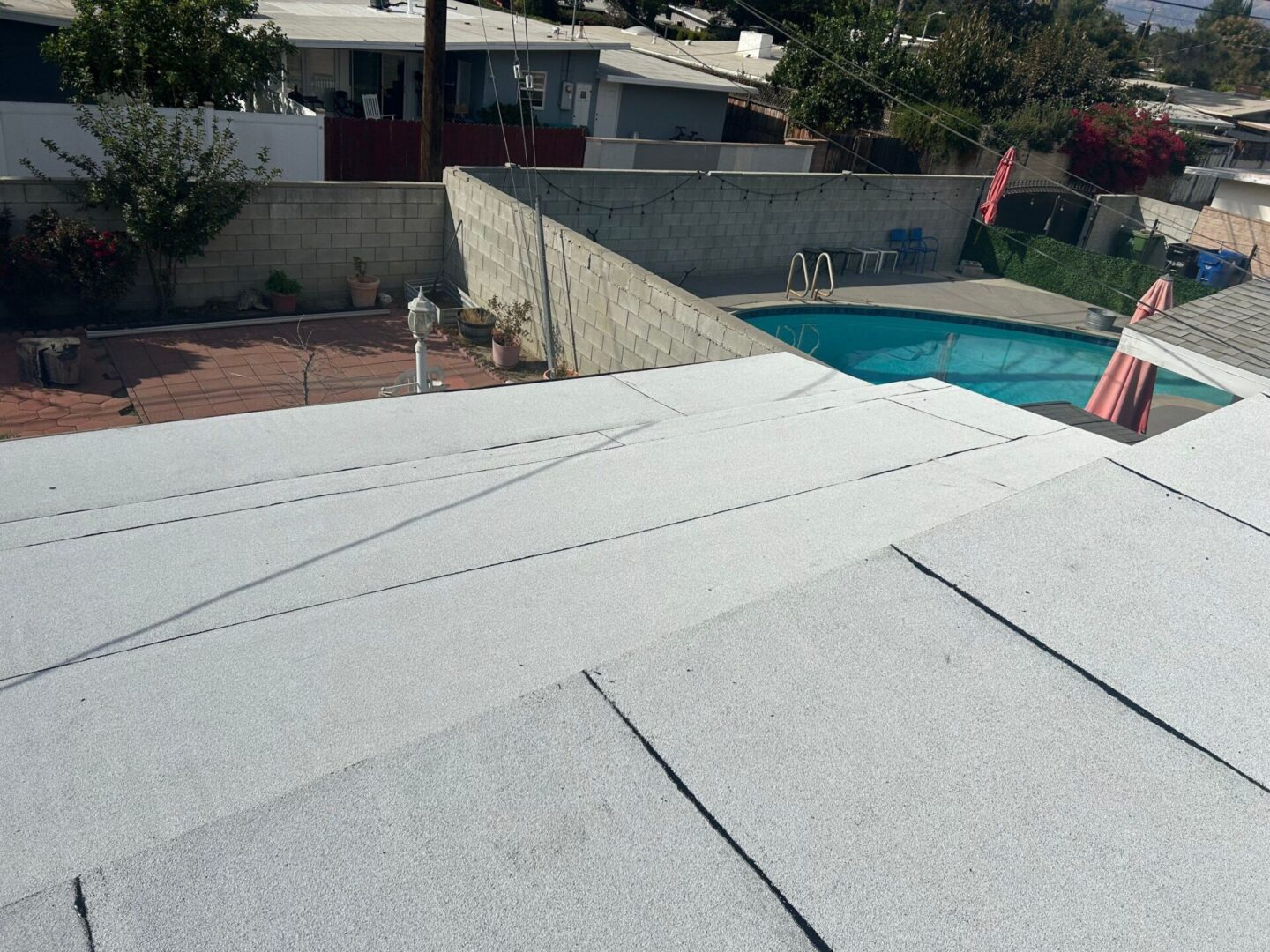 Roofing work in progress with white shingles near a backyard pool.