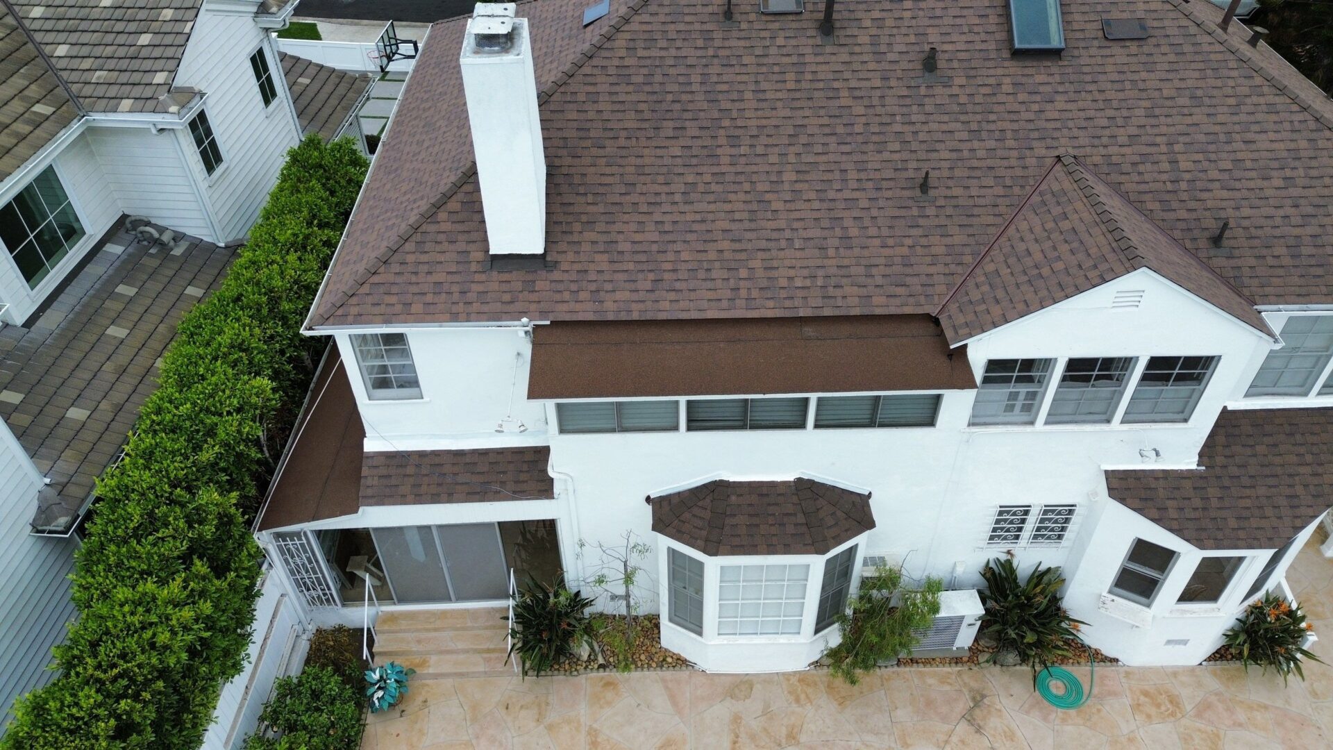 A white multi-story house with a brown roof and bay window.