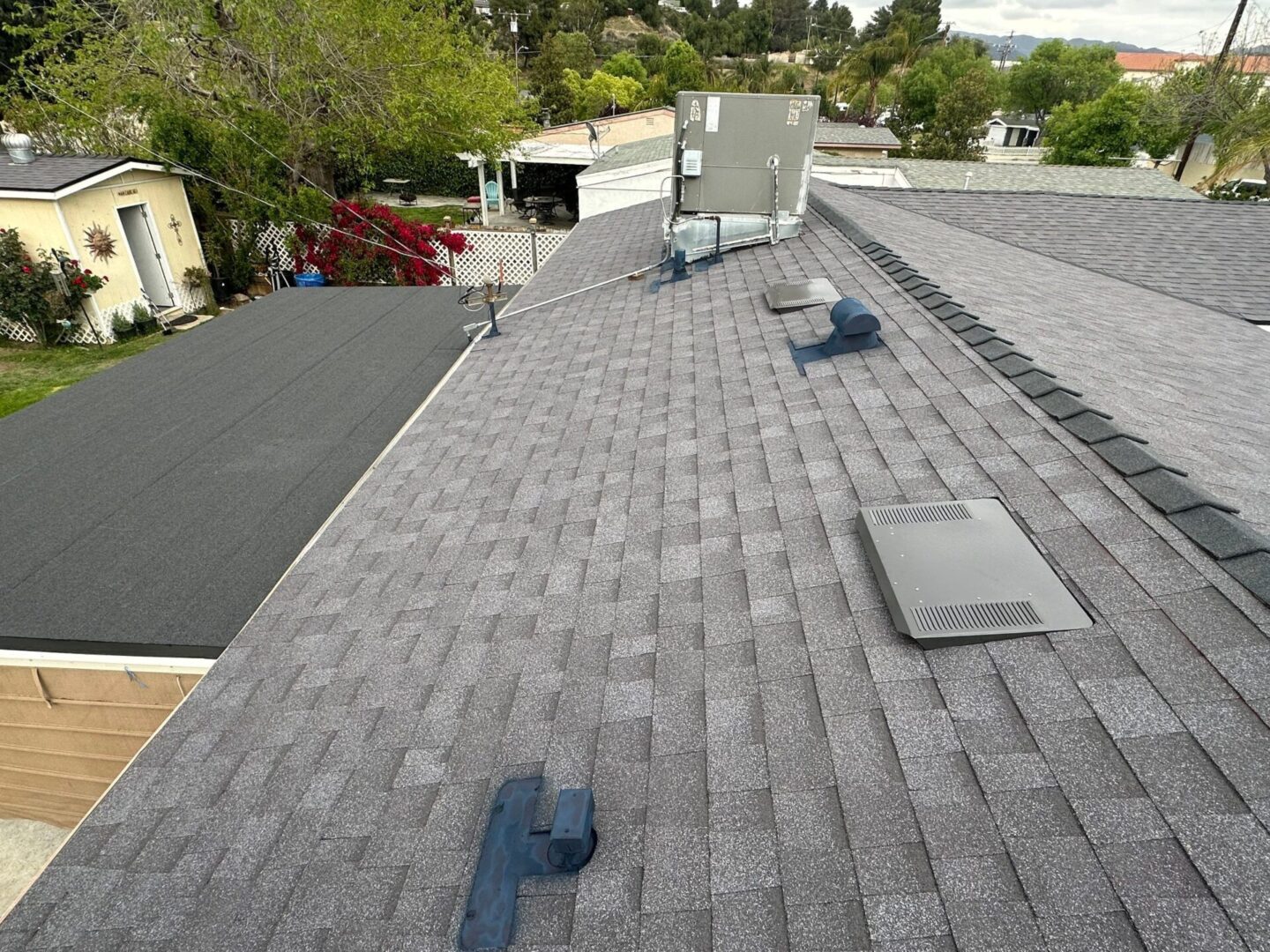 A rooftop with gray shingles and several vents under a cloudy sky.
