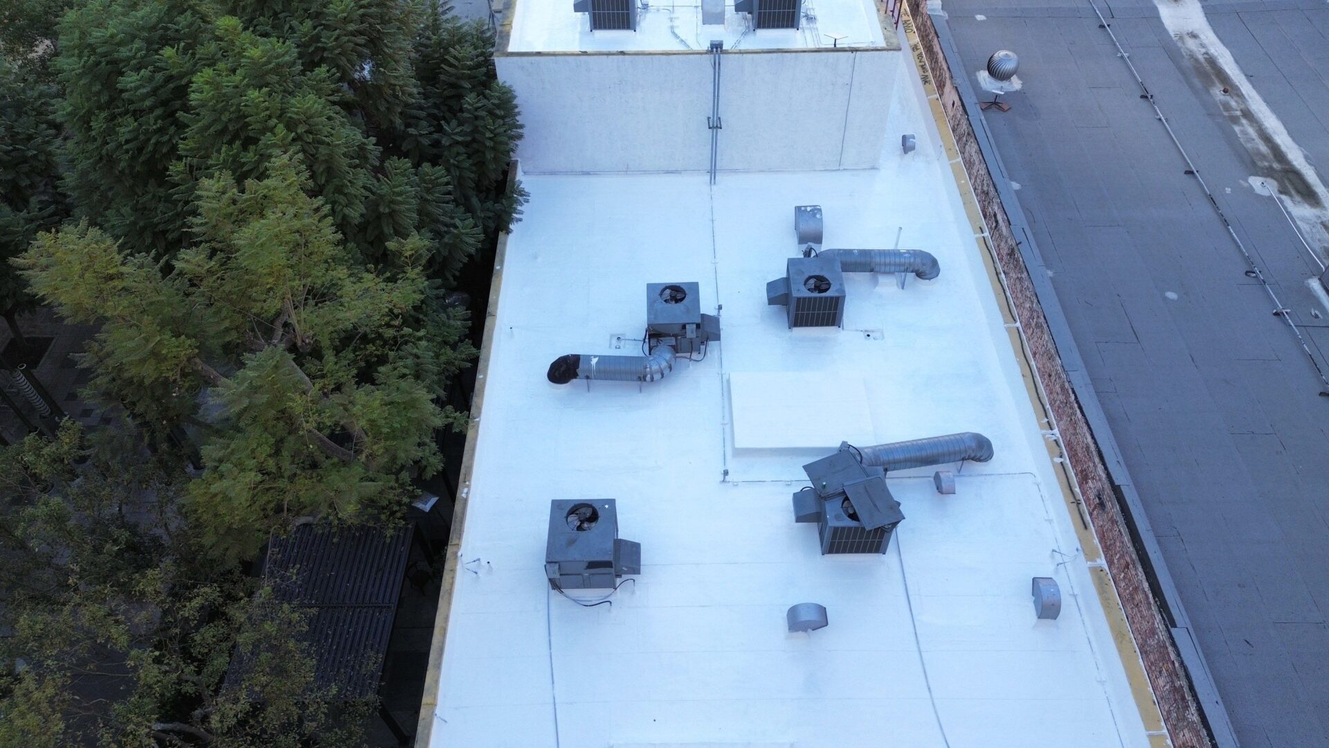 A rooftop with ventilation units and greenery nearby.
