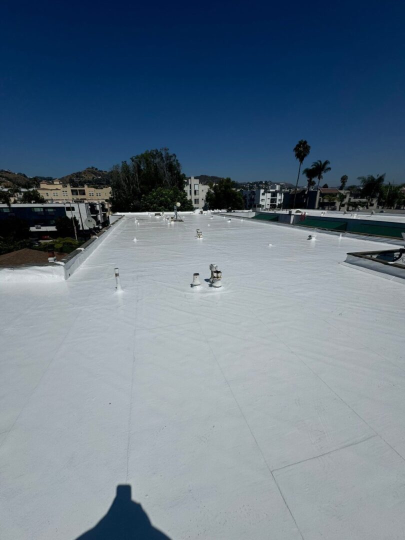 A large flat roof coated with white reflective material under clear blue sky.
