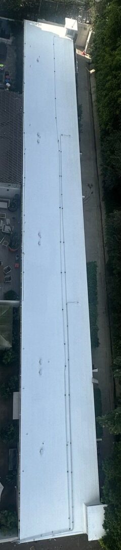 A rooftop view showing a white roof with pipes and a parking lot beside it.