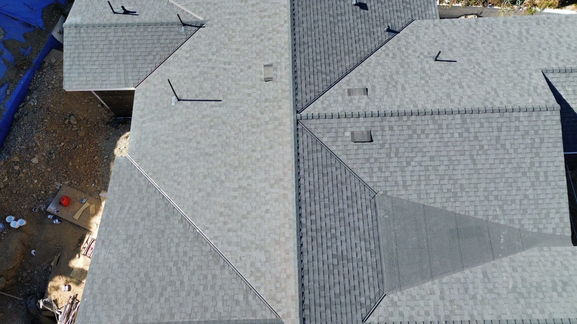 Aerial view of adjacent gray shingled rooftops with vents and shadows.