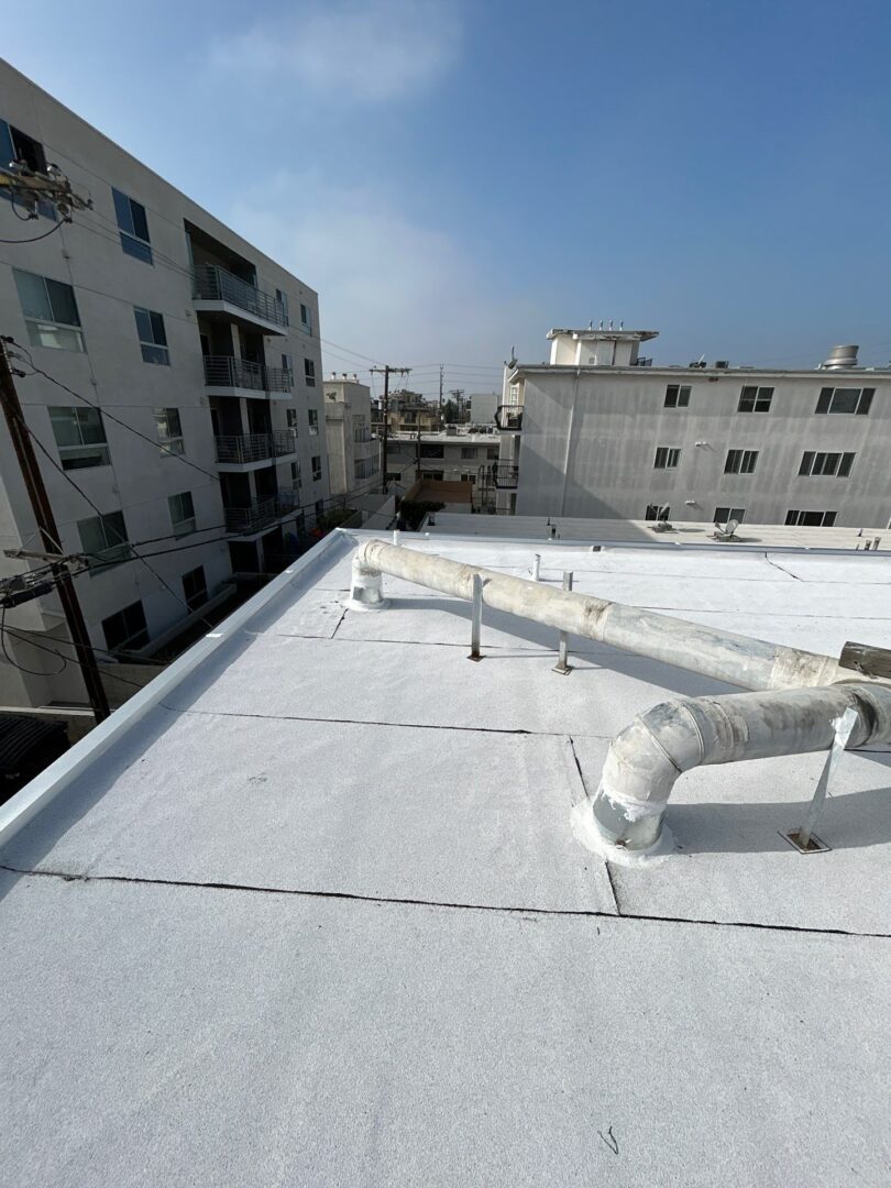 Flat white-painted rooftop with ventilation pipes in an urban setting.