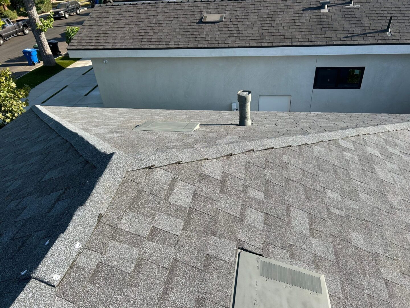 View of a shingled rooftop with a chimney and neighboring building.