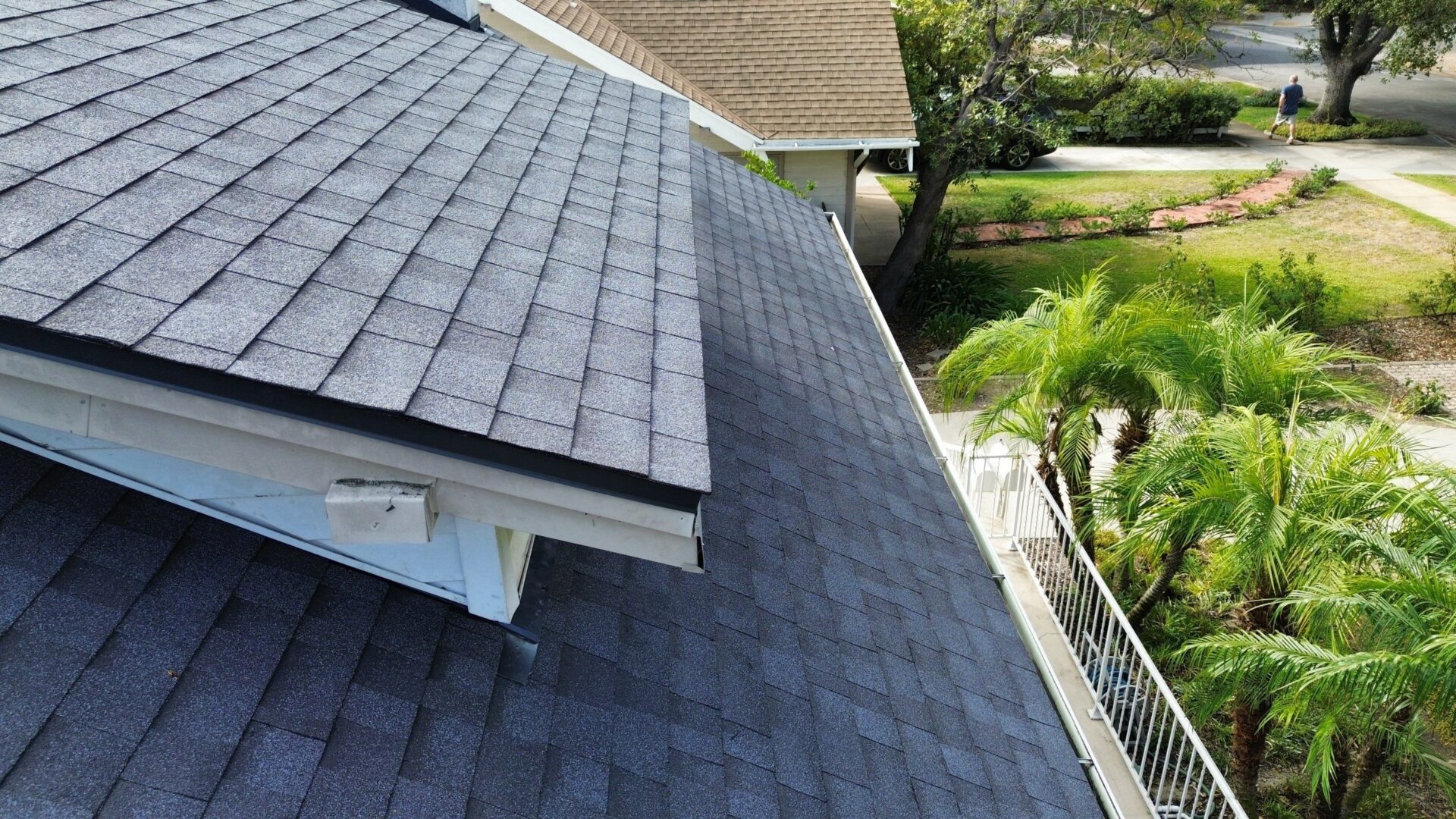 View of a dark gray shingled roof with a garden in the background.
