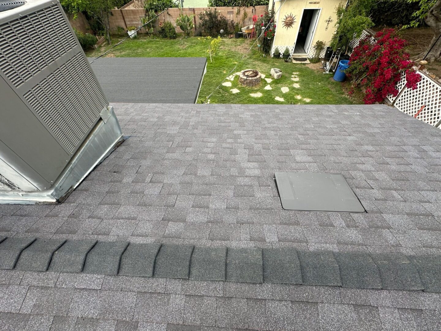 A gray shingled roof with a hatch and a grassy backyard.