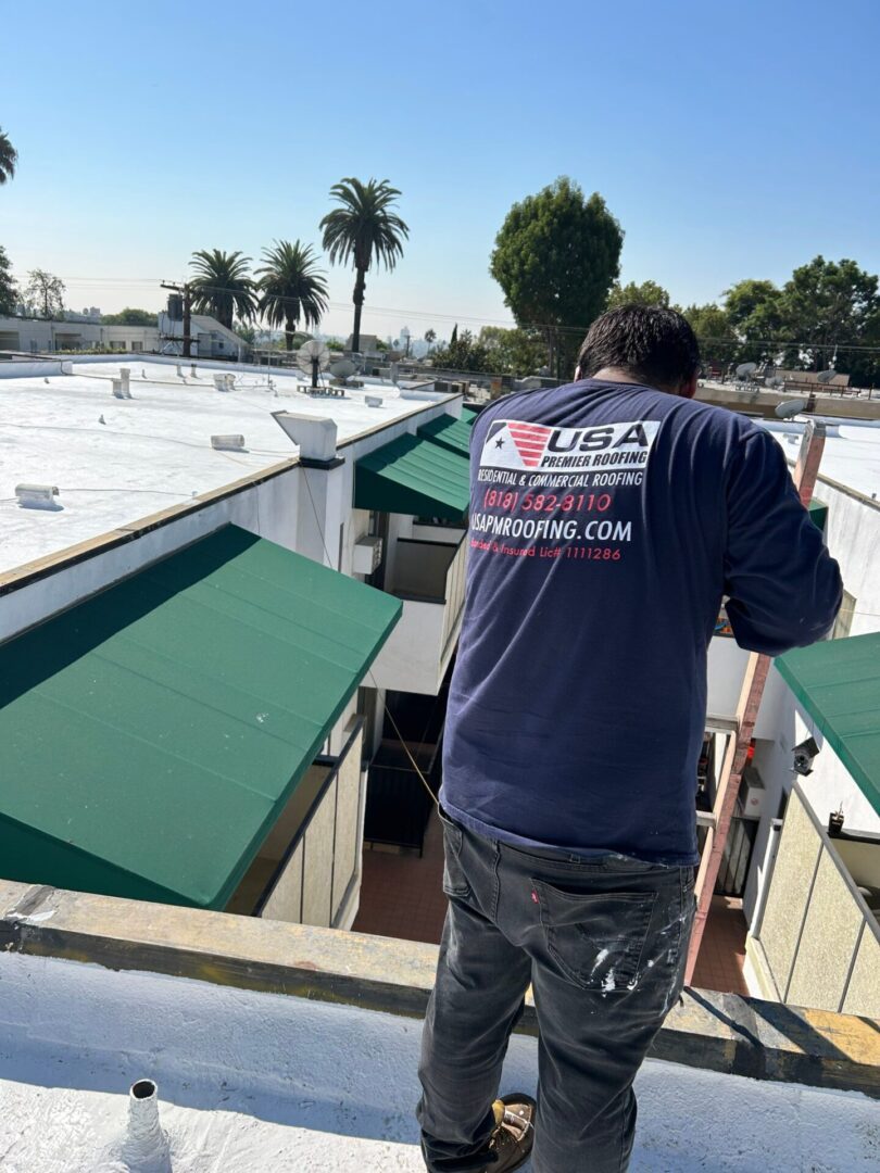 A worker on a roof wearing a USA Solar shirt near green awnings.