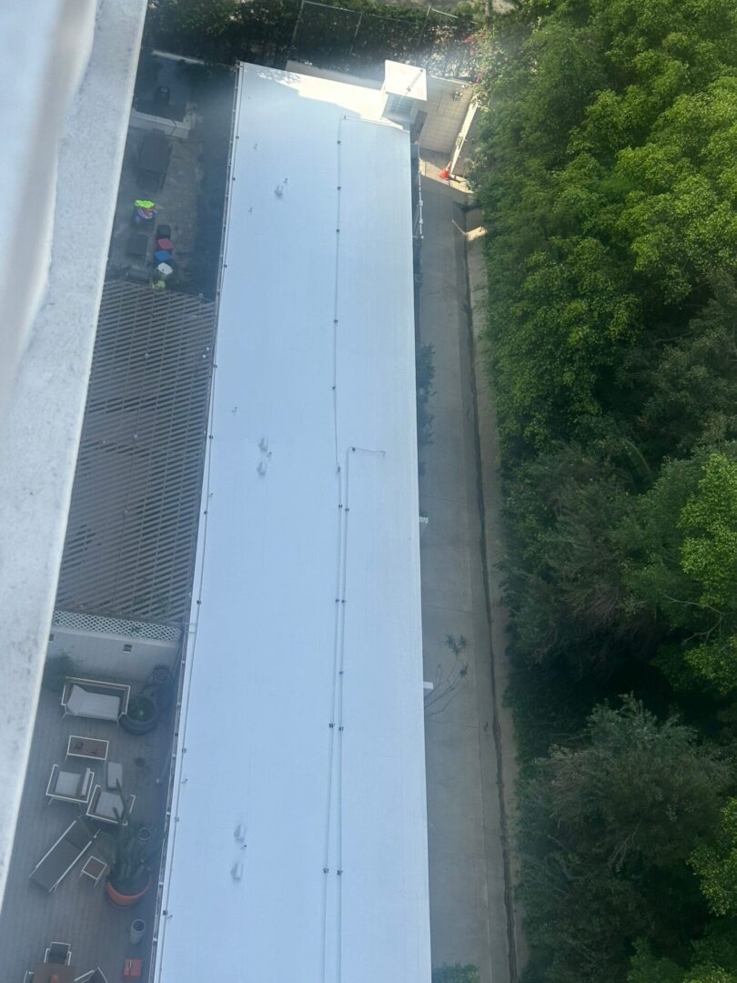 Aerial view of a long white rooftop next to green trees.
