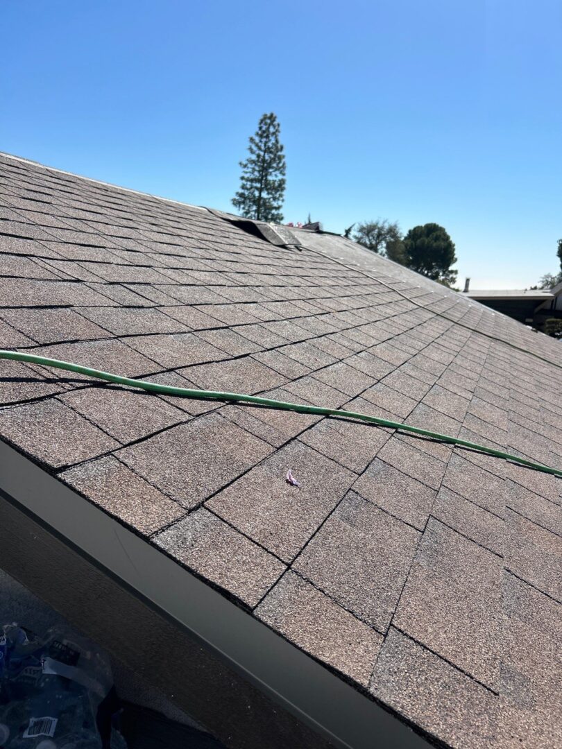 A rooftop with asphalt shingles and ropes laid across it under a clear sky.