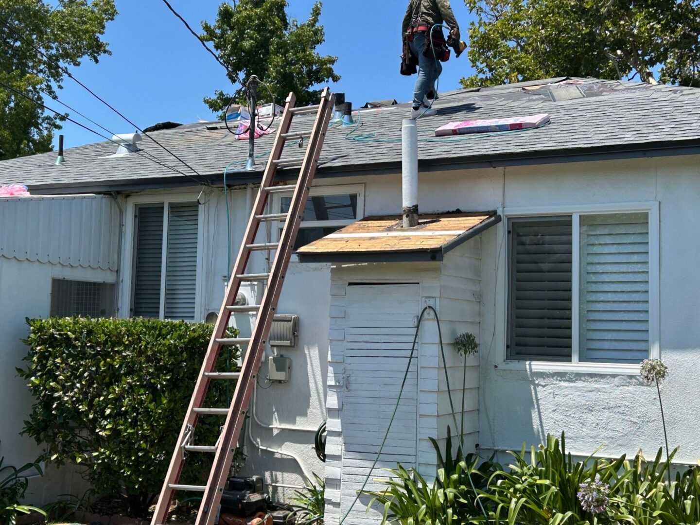Two workers repair a roof on a sunny day with ladders and safety gear.