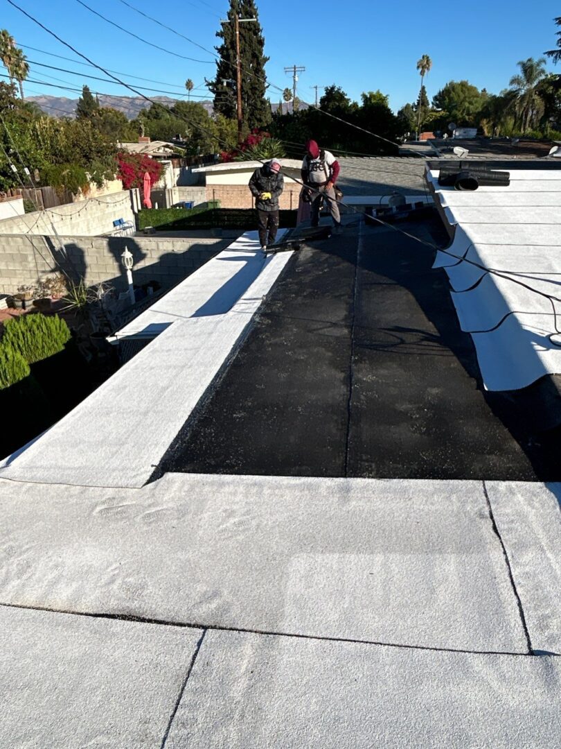 Workers applying roofing materials on a flat roof under clear sky.