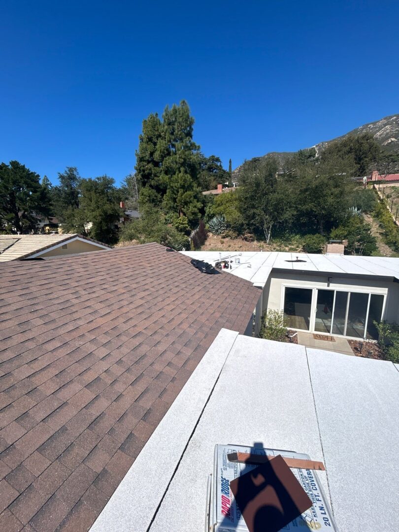 View from rooftop showing shingles, trees, and clear sky.