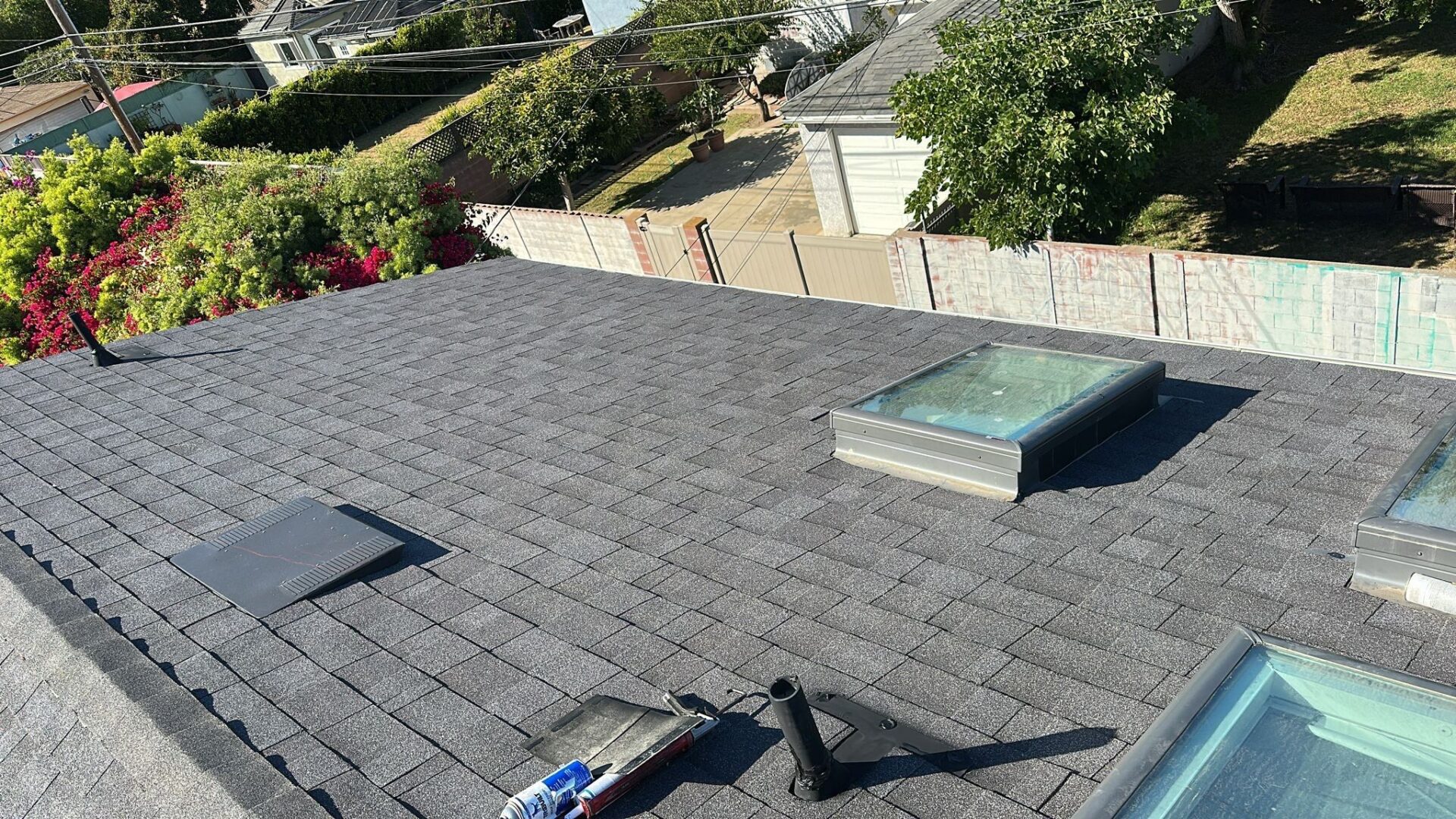 Newly installed rooftop shingles with skylights and roofing tools visible.
