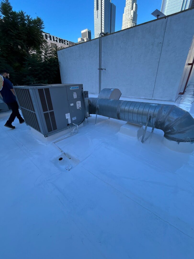A person walking near a large HVAC duct on a snowy rooftop.