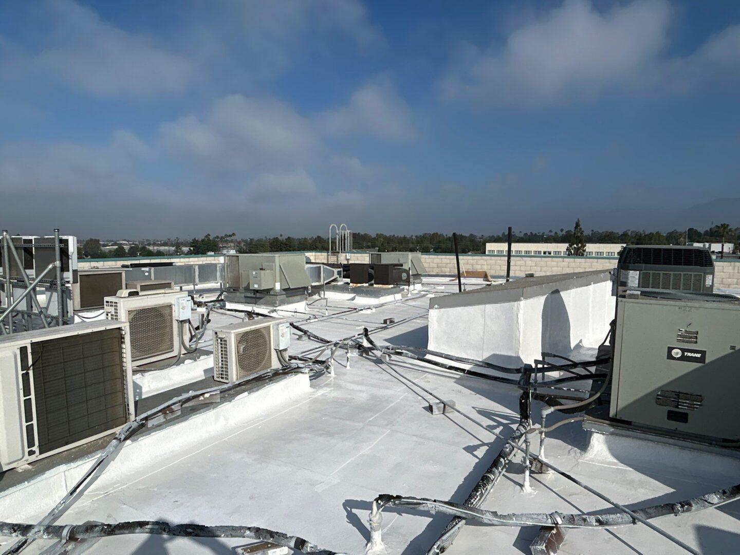 Rooftop with white waterproof coating and HVAC units under a partly cloudy sky.