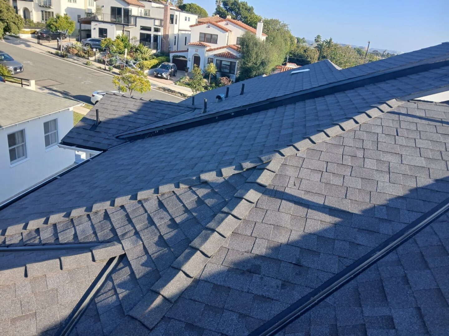 A sunny rooftop with gray shingles casting shadows in a residential area.