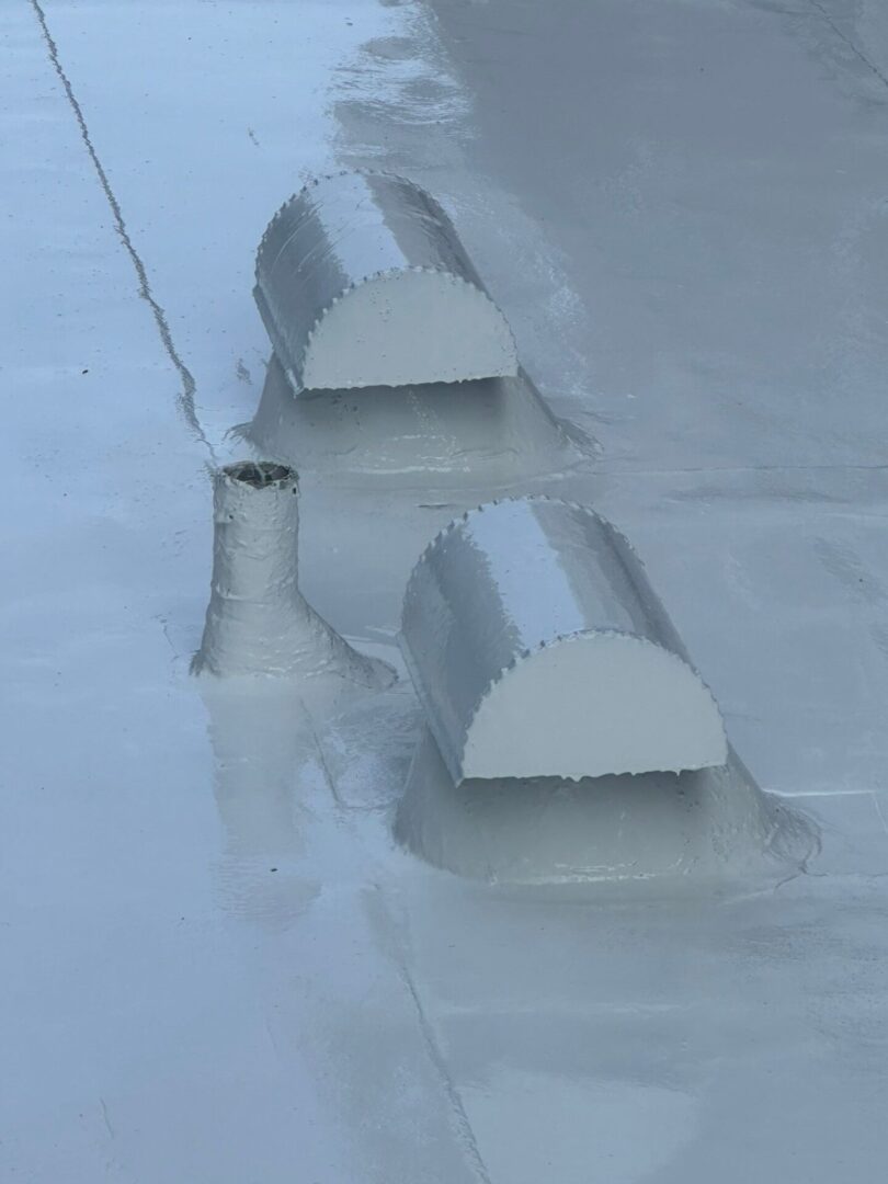 Two gray roof vents on a flat rooftop with a smooth surface.