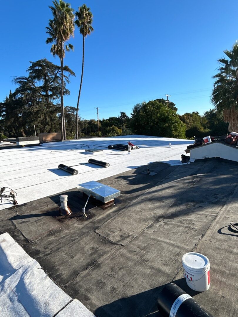 Workers installing white roofing material on a flat roof under clear blue sky.
