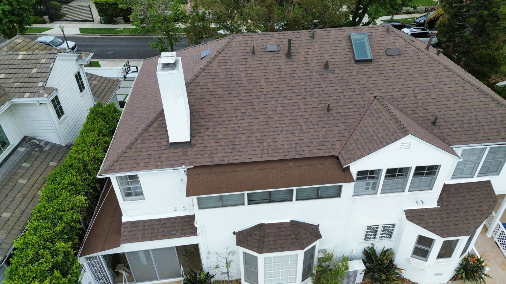 Aerial view of a white house with a brown shingled roof and multiple chimneys.