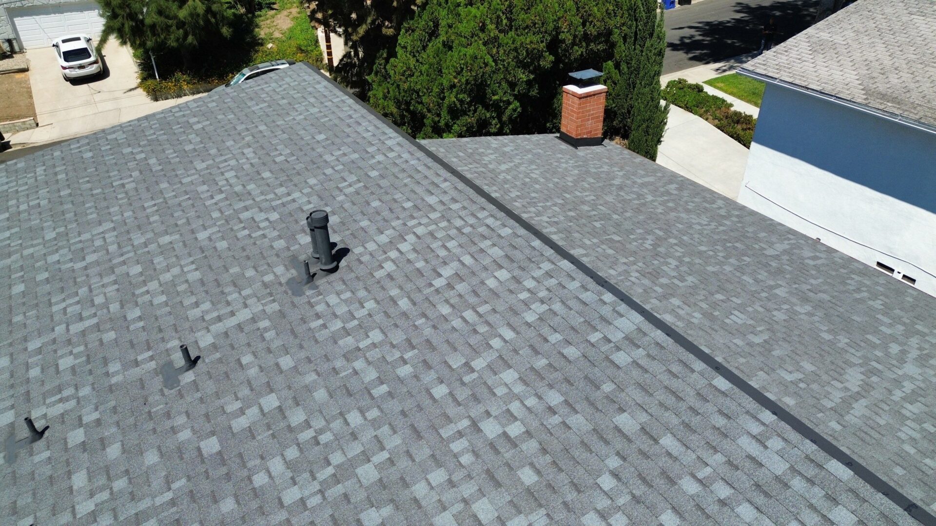 A rooftop with gray shingles and two chimneys under a clear sky.